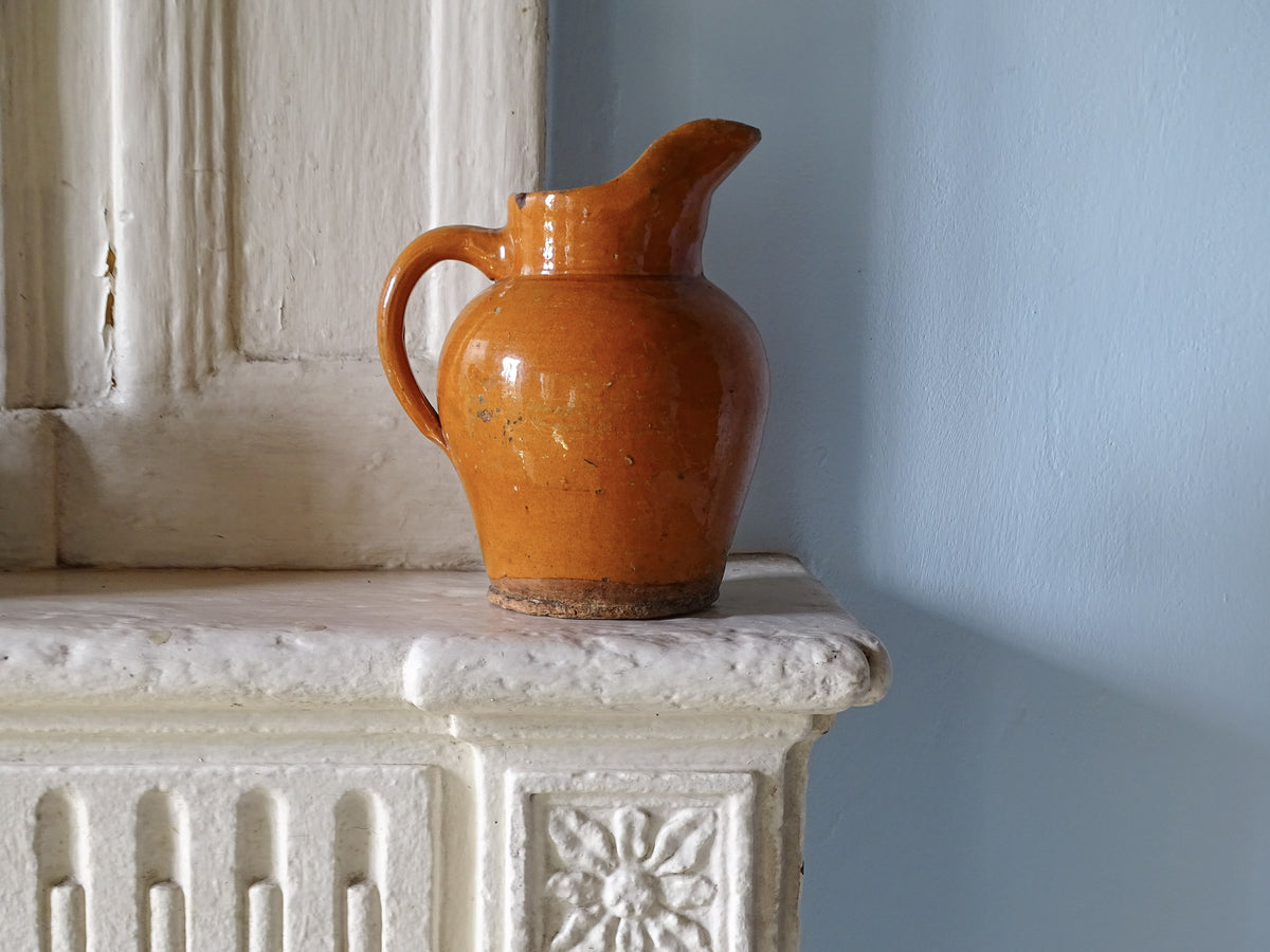 French antique ceramic pitcher with orange glaze on country house fireplace