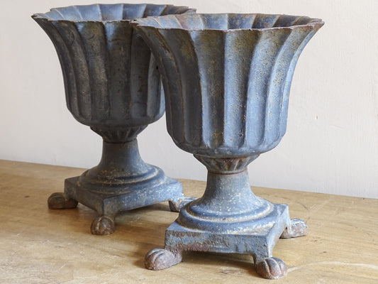 A sculptural pair of French antique cast iron urn planters, with fluted bowls set on stepped bases and raised on paw feet. These antique planters date to to the latter part of the 19th century. They have developed a deep, dark patina.
