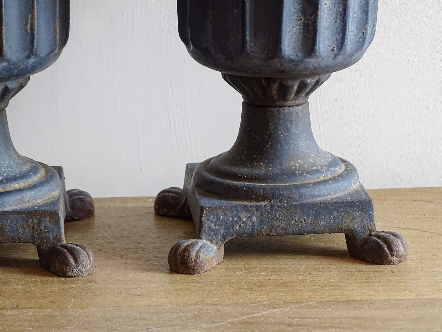 A sculptural pair of French antique cast iron urn planters, with fluted bowls set on stepped bases and raised on paw feet. These antique planters date to to the latter part of the 19th century. They have developed a deep, dark patina.