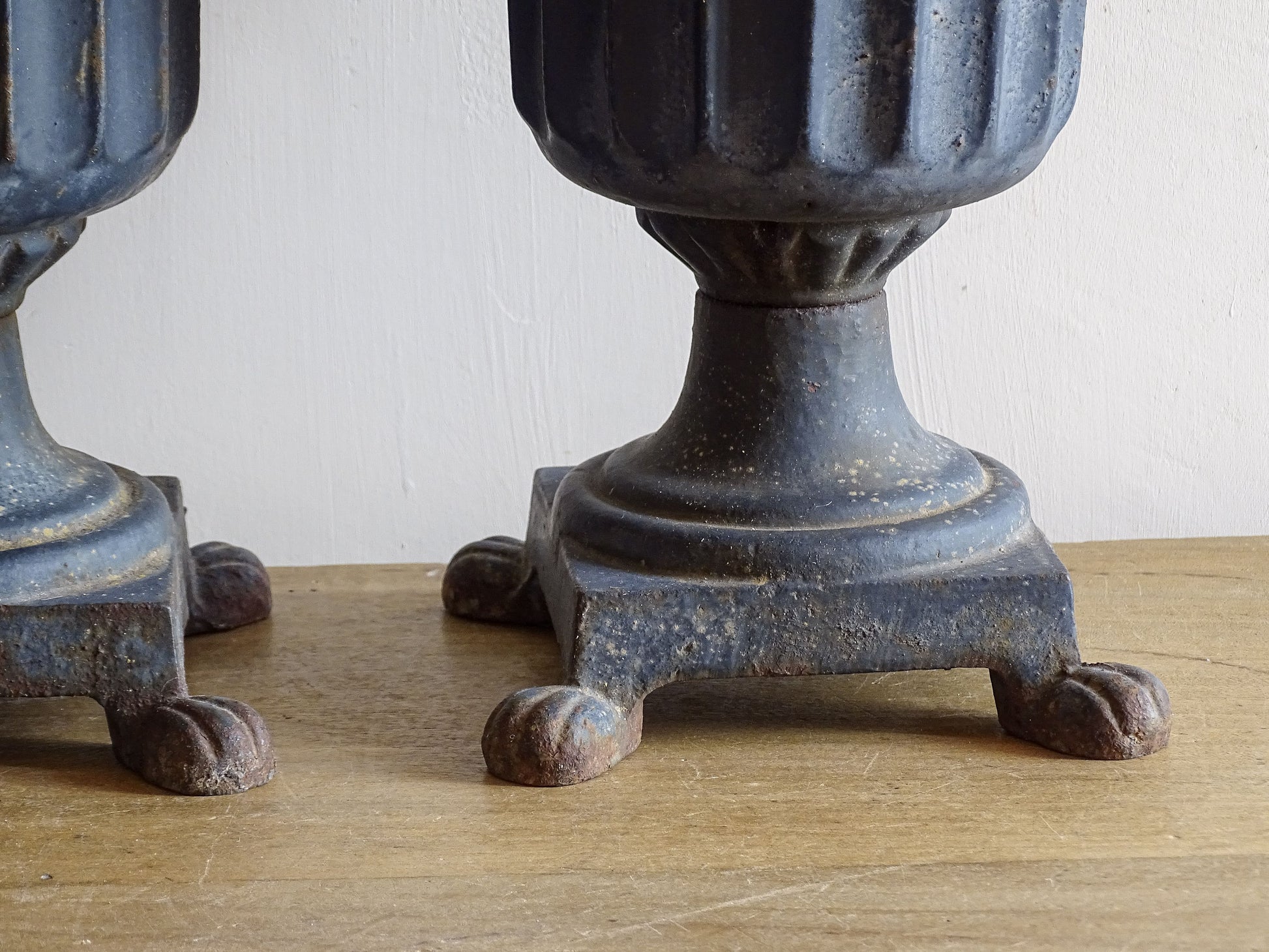 A sculptural pair of French antique cast iron urn planters, with fluted bowls set on stepped bases and raised on paw feet. These antique planters date to to the latter part of the 19th century. They have developed a deep, dark patina.