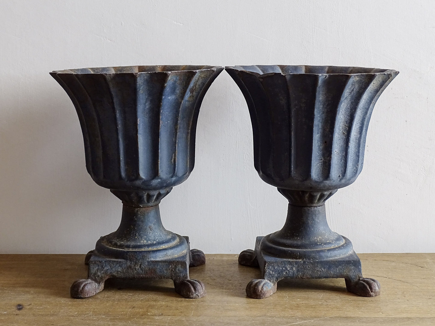 A sculptural pair of French antique cast iron urn planters, with fluted bowls set on stepped bases and raised on paw feet. These antique planters date to to the latter part of the 19th century. They have developed a deep, dark patina.