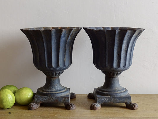 A sculptural pair of French antique cast iron urn planters, with fluted bowls set on stepped bases and raised on paw feet. These antique planters date to to the latter part of the 19th century. They have developed a deep, dark patina.