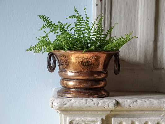 French antique hammered copper planter with wrought iron handles and a fern. Pictured on a country house fireplace next to a pale blue wall