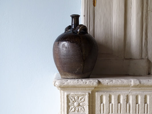 French antique earthenware pitcher with a dark brown glaze, pictured on a country house fireplace mantel