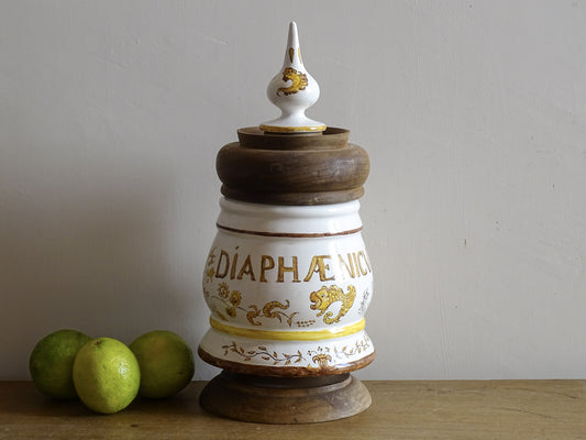 A vintage ceramic apothecary jar with hand-painted decoration and gilt lettering, with a wooden lid and base. Inspired by traditional European pharmacy vessels
