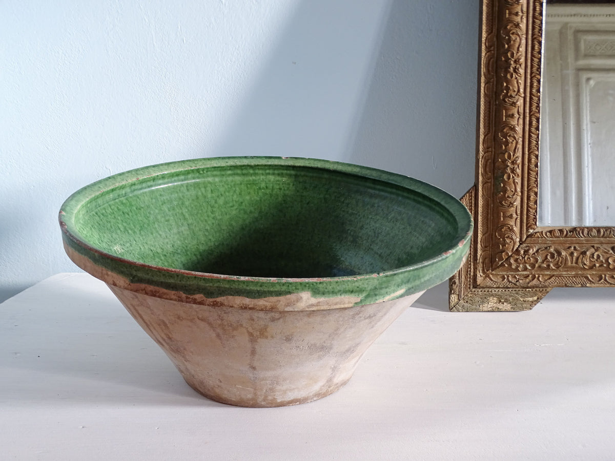 French antique tian bowl with a green glaze interior and unglazed earthenware exterior. Pictured next to a gold mirror in front of a pale blue wall