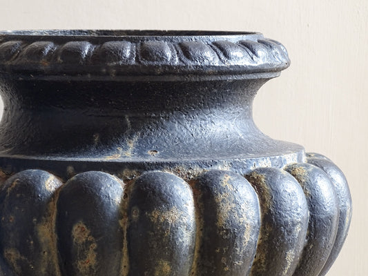 A pair of French antique cast iron garden urns, dating to the late 19th century. Cast in a classic campana form, each urn features a deeply gadrooned body, a softly moulded rim and a stepped pedestal base.