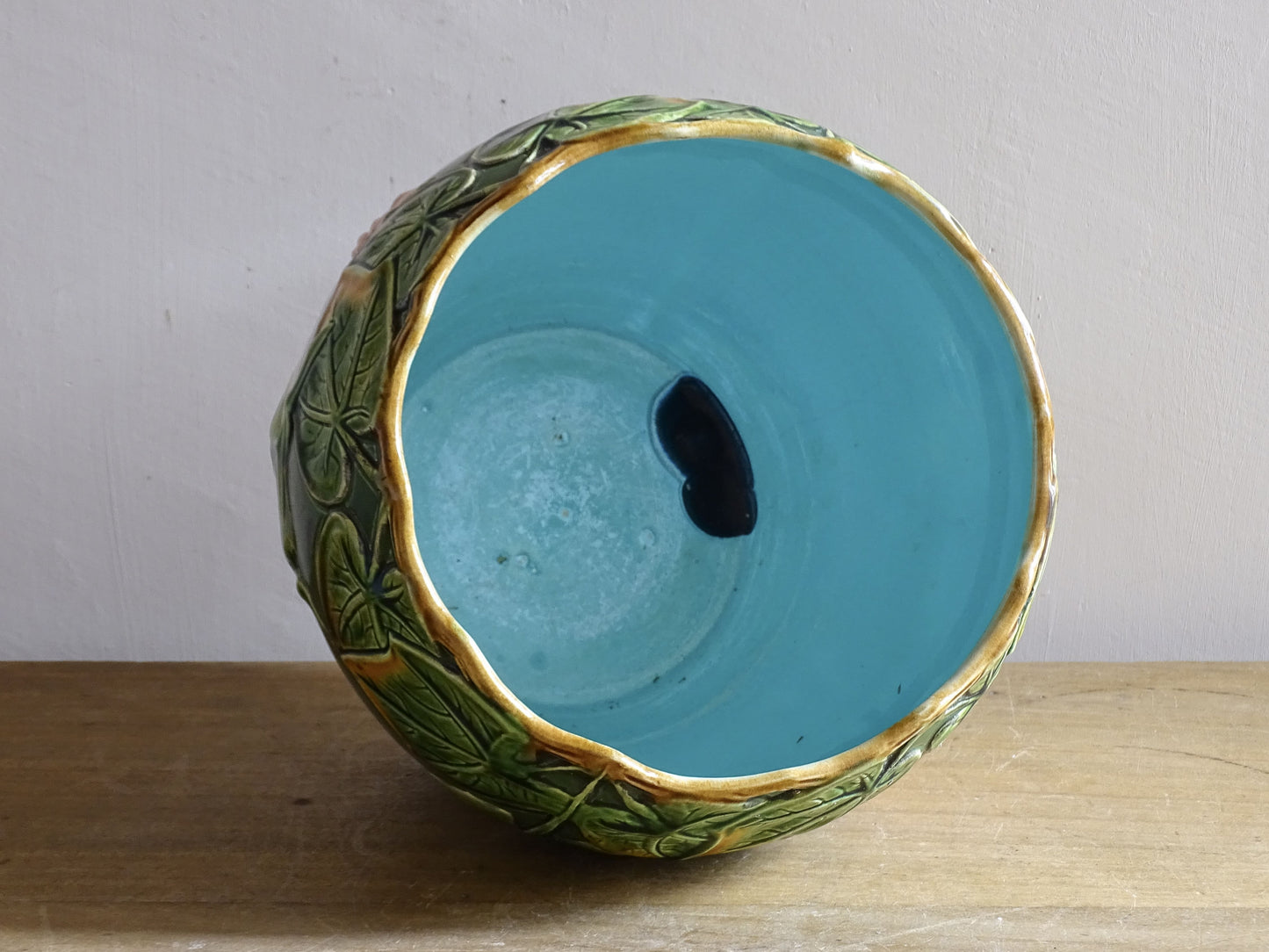 An antique ceramic cache pot dating to the turn of the 20th century, with strong Art Nouveau influence. The planter is richly decorated in relief, with trailing ivy leaves encircling the rim and a flowing trumpet-shaped flower applied to the body.
