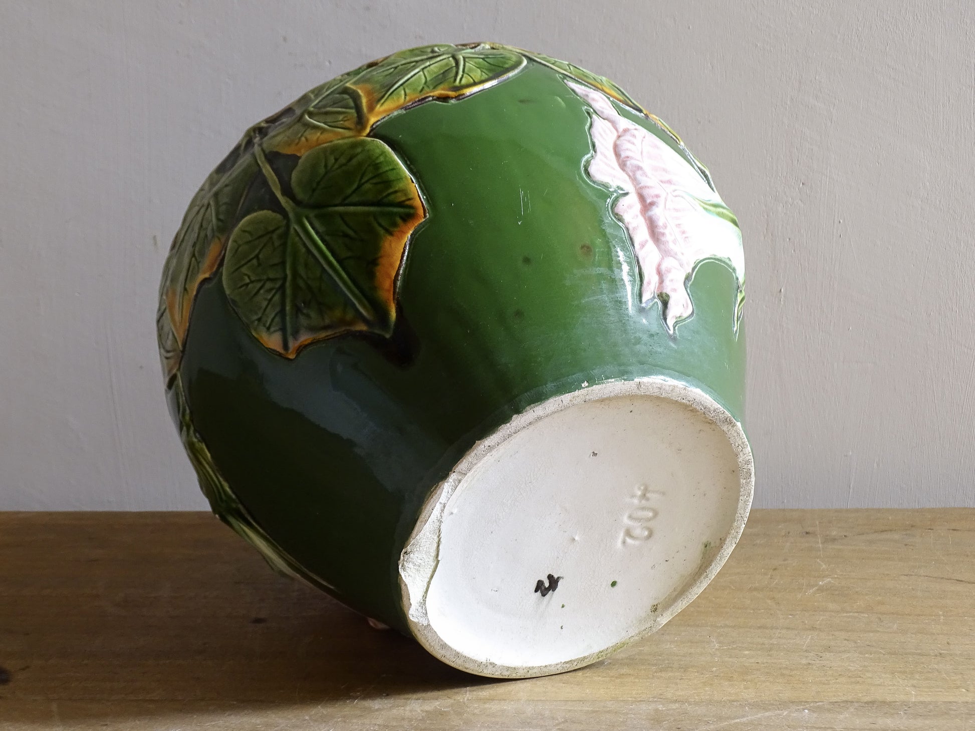An antique ceramic cache pot dating to the turn of the 20th century, with strong Art Nouveau influence. The planter is richly decorated in relief, with trailing ivy leaves encircling the rim and a flowing trumpet-shaped flower applied to the body.