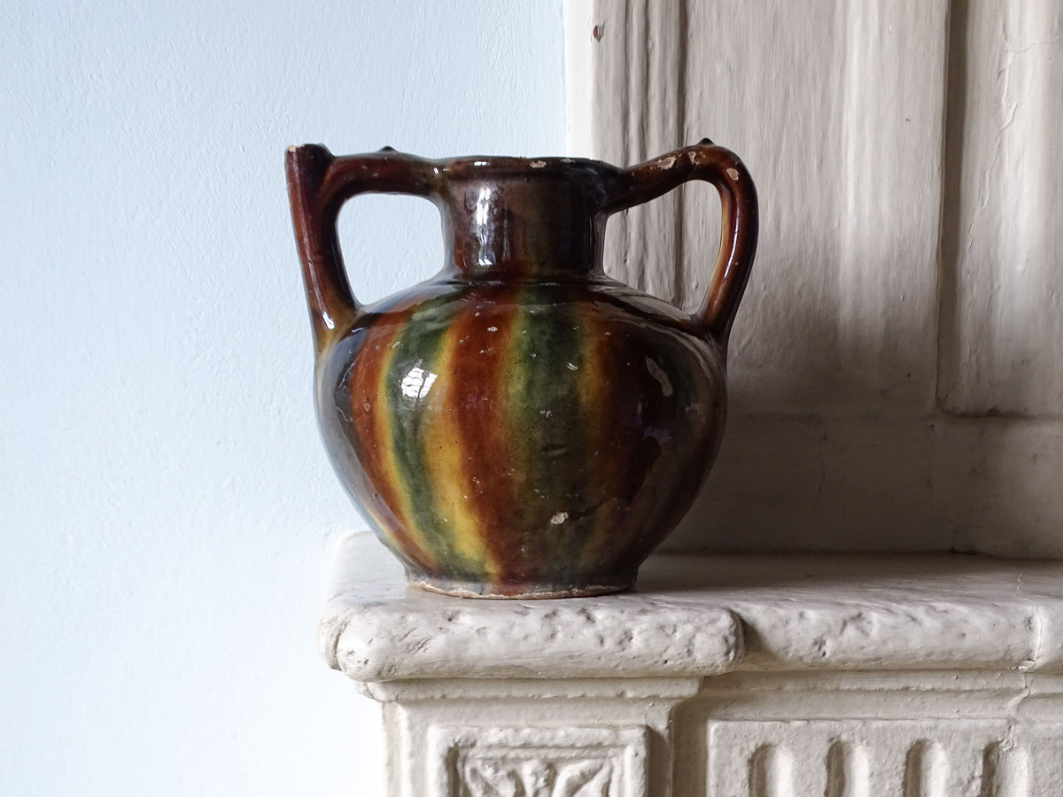 French antique ceramic pitcher or orjol with a striped glaze in brown, blue and yellow. Pictured on a country house fireplace.