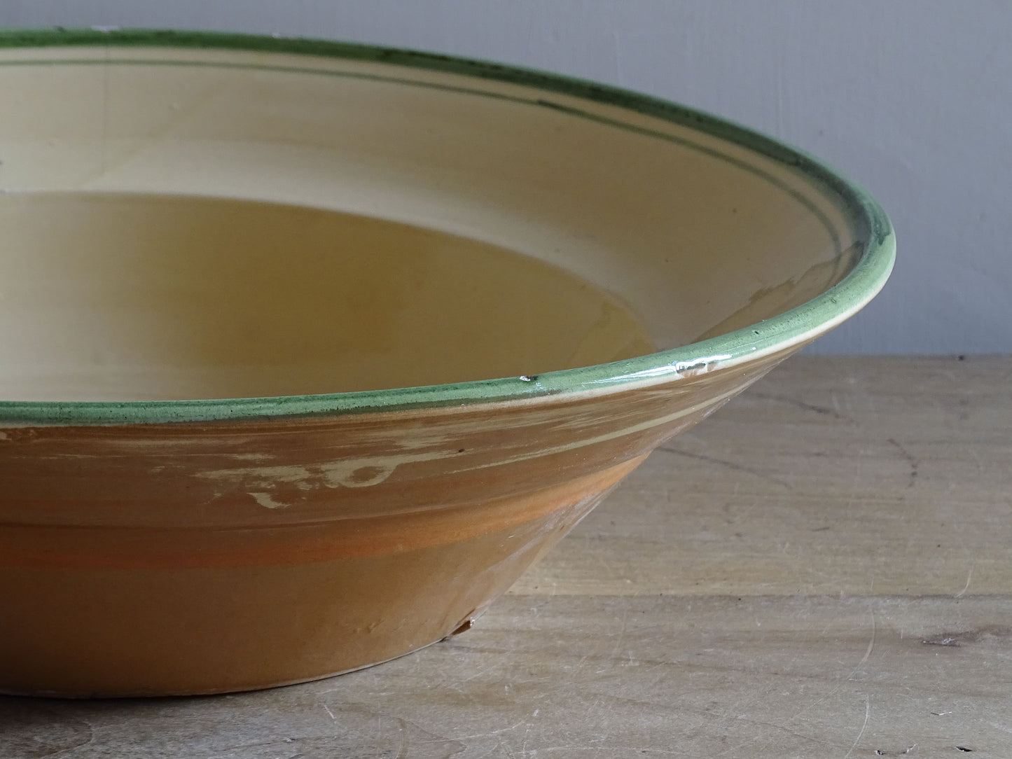   A large French  vintage  bowl  made from glazed terracotta with a warm honey-toned exterior, a soft cream glazed interior and a traditional green rim. 