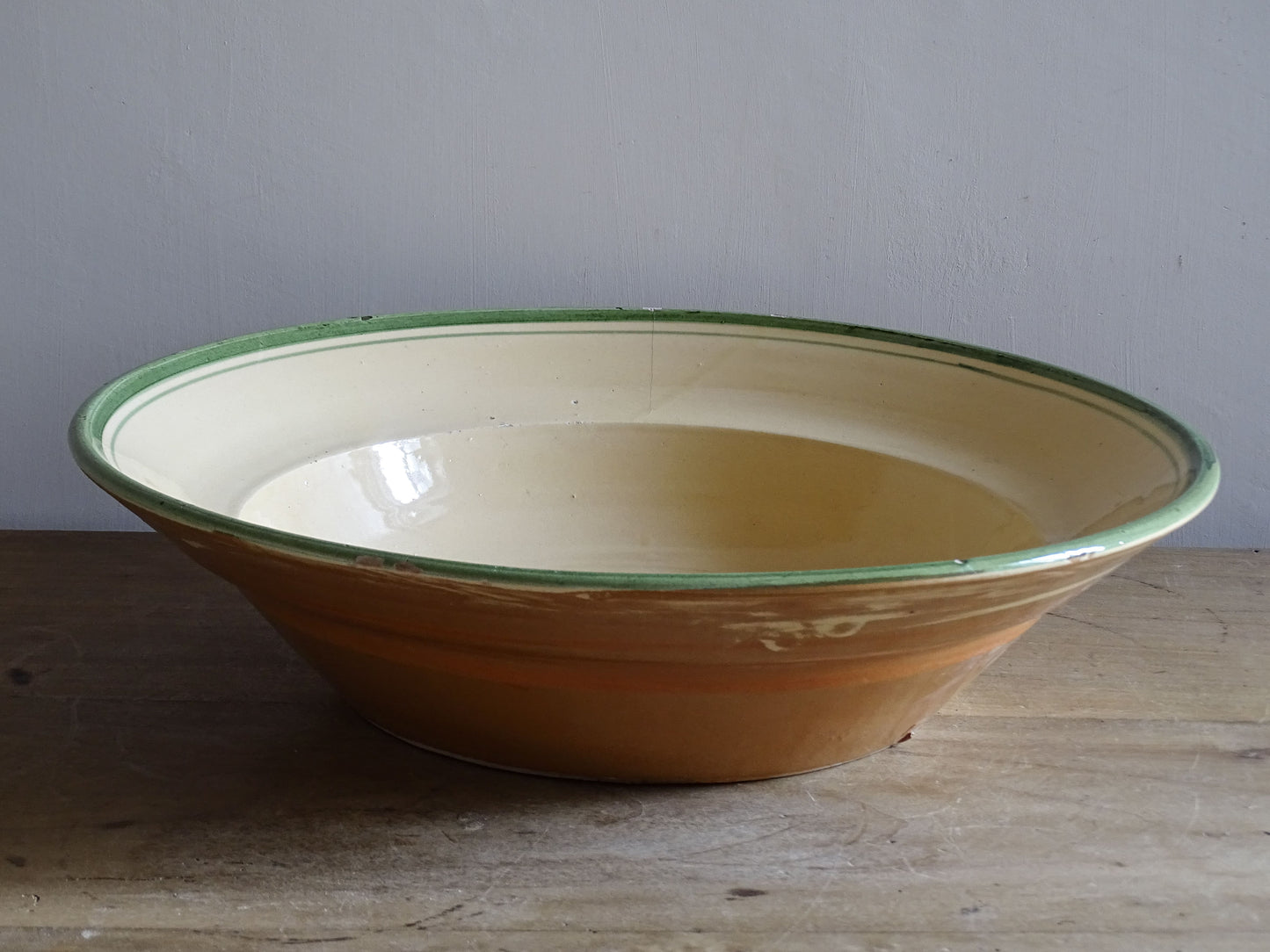   A large French  vintage  bowl  made from glazed terracotta with a warm honey-toned exterior, a soft cream glazed interior and a traditional green rim. 
