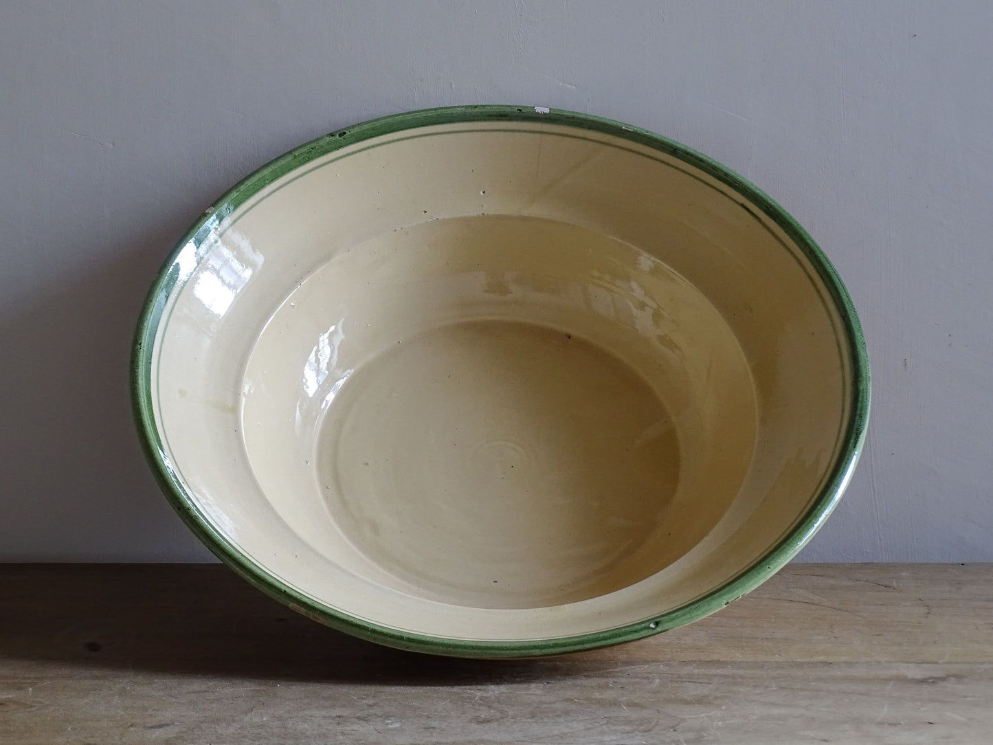   A large French  vintage  bowl  made from glazed terracotta with a warm honey-toned exterior, a soft cream glazed interior and a traditional green rim. 