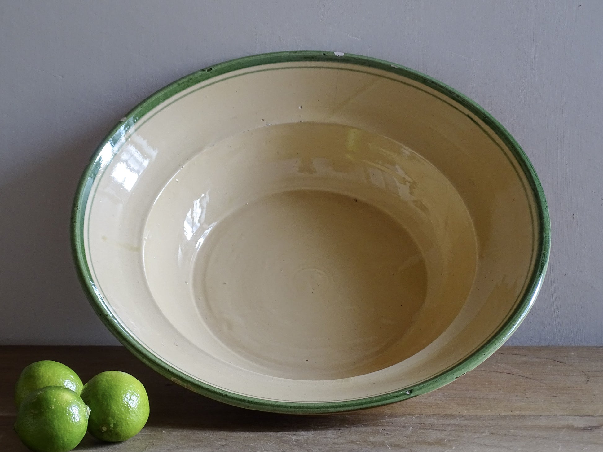   A large French  vintage  bowl  made from glazed terracotta with a warm honey-toned exterior, a soft cream glazed interior and a traditional green rim. 