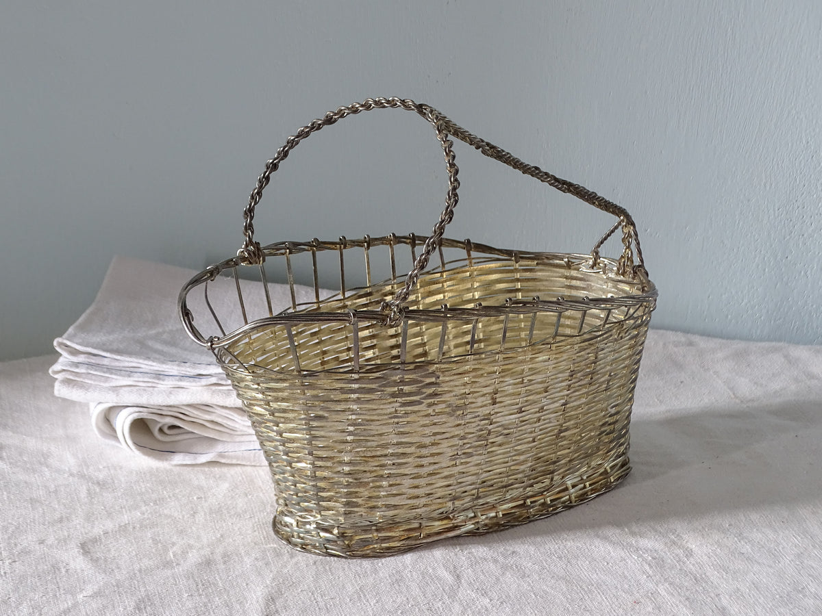 A French vintage woven metal basket bottle carrier with a twisted metal handle.