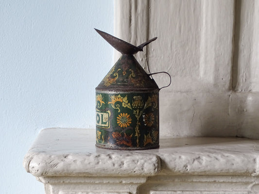 A French antique lithographed metal jug decorated with floral patterns in yellow, orange, and green. Pictured on a stone mantelpiece against a light blue wall in a country house.