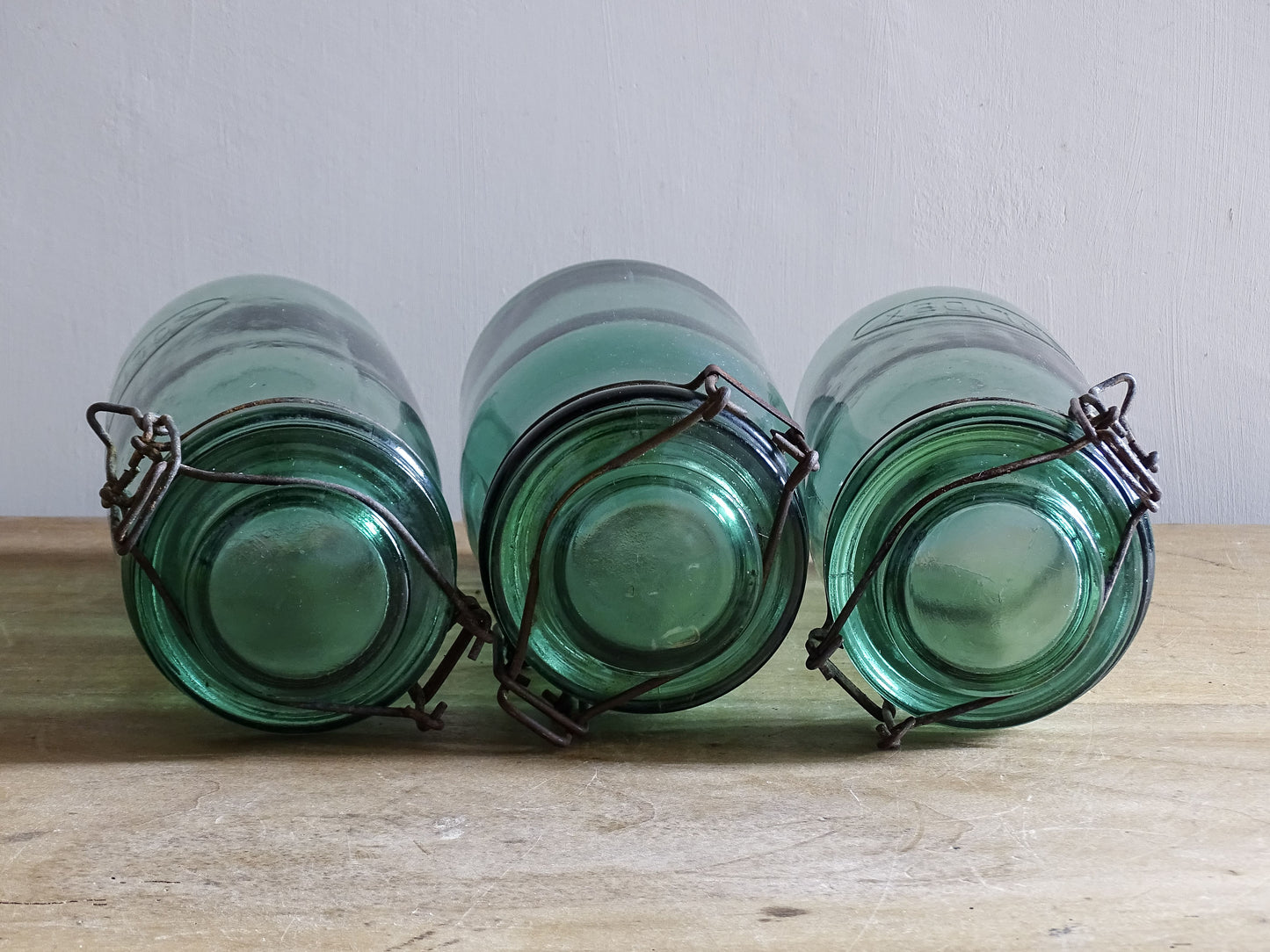 Three green glass jars with metal clasps on a wooden surface.