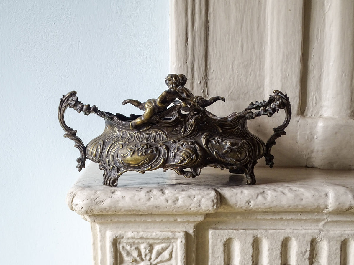 An ornate French antique art nouveau planter with cherubs, displayed on a country house fireplace
