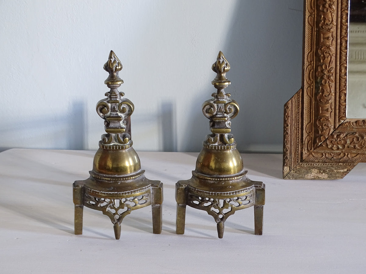 French antique brass andirons or firedogs with gothic detailing pictured next to a gold mirror
