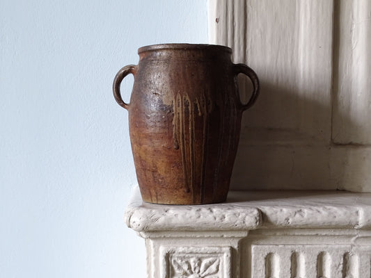 French antique earthenware pot with two handles and dark brown glaze, pictured on a country house fireplace