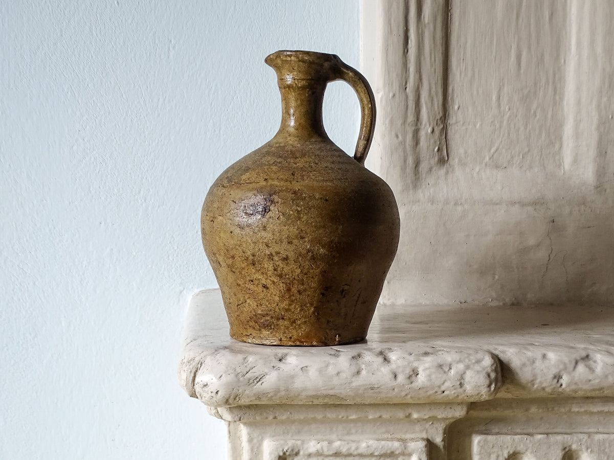 Rustic French antique ceramic pitcher with brown glaze, pictured on a country house fireplace