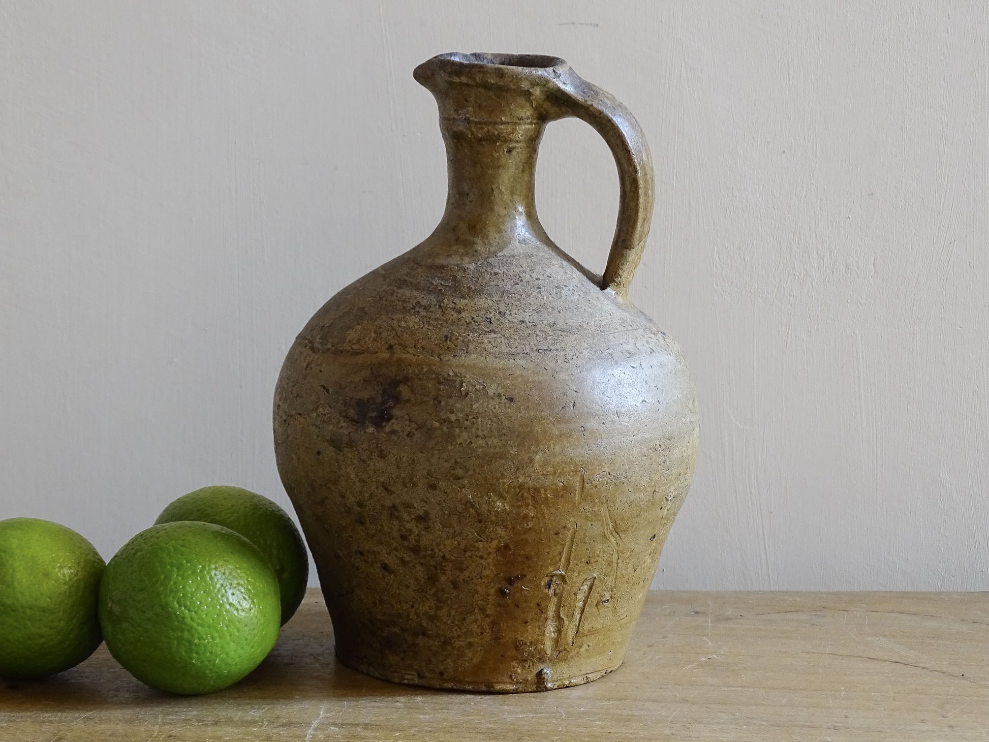 Small French antique pottery pitcher with warm honey glaze on wooden table