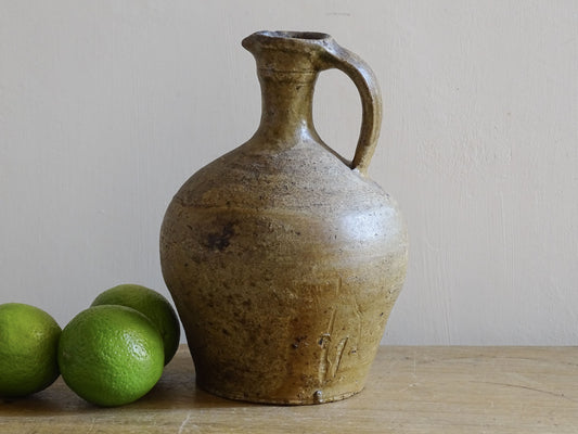 Small French antique pottery pitcher with warm honey glaze on wooden table