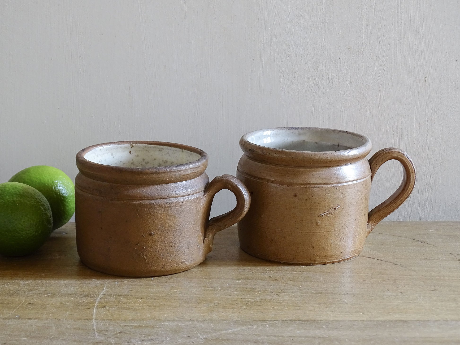 Pair of rustic French vintage stoneware mugs with ribbed handles on wooden table