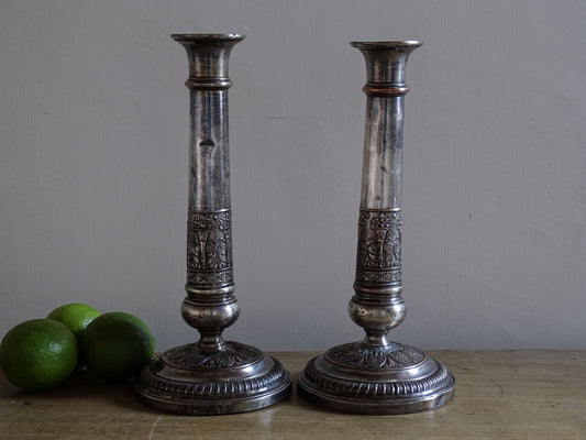 Pair of French antique silver-plated candlesticks with decorative repoussé detailing on a rustic wooden table