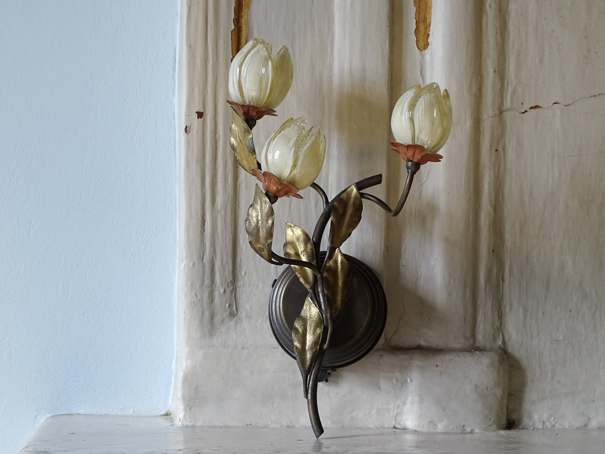 A vintage Italian wall sconce with three tulip-shaped glass shades and metallic gold-toned leaves on a dark metal stem by L'originale