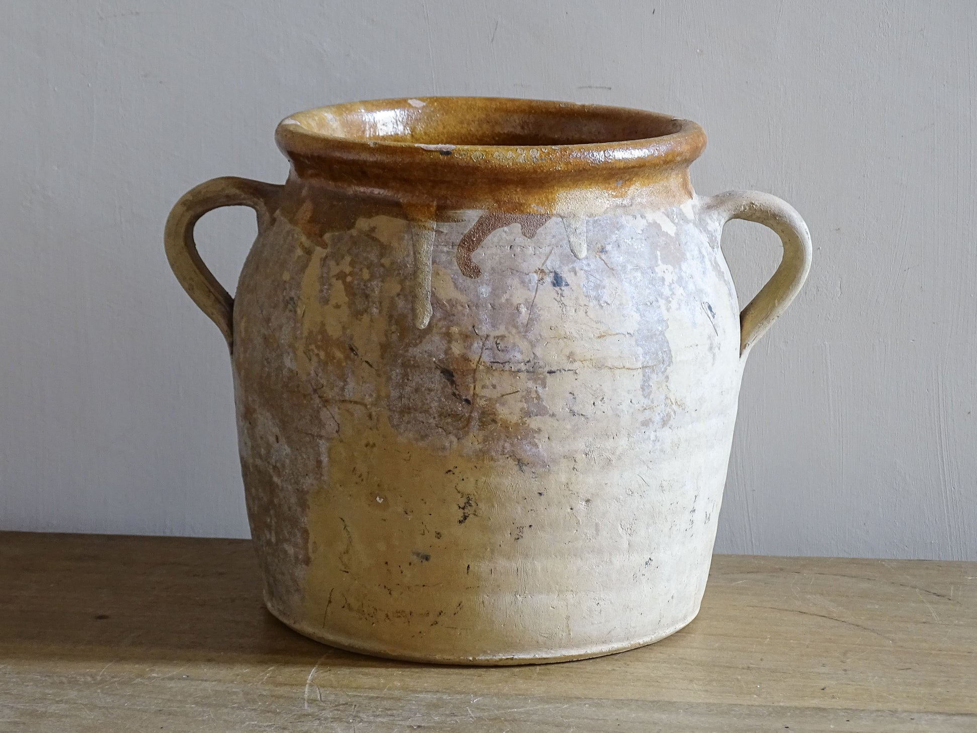 Rustic French confit pot displayed on wooden table with warm honey glaze interior