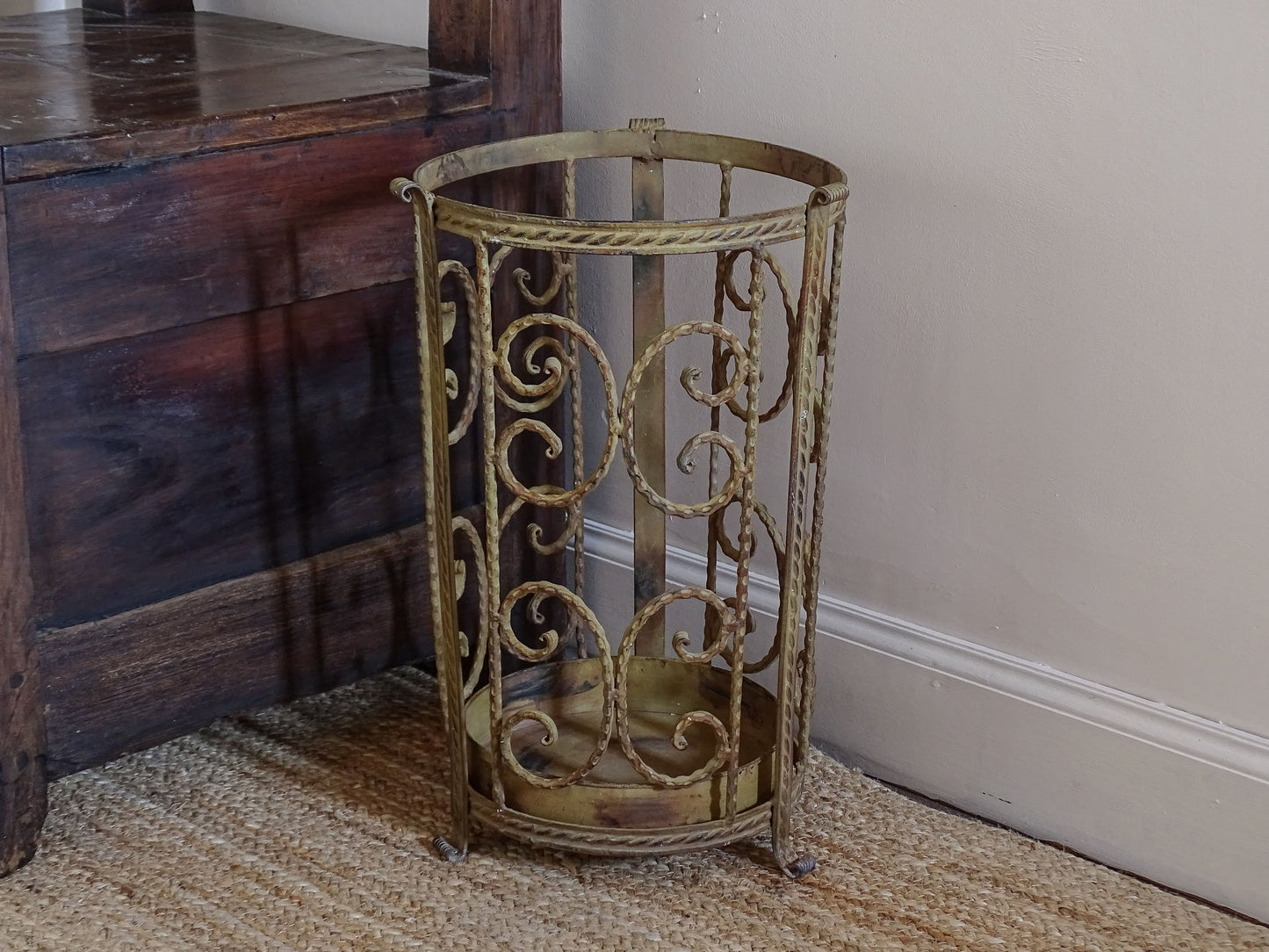 Decorative French umbrella stand in distressed painted metal beside rustic wooden furniture
