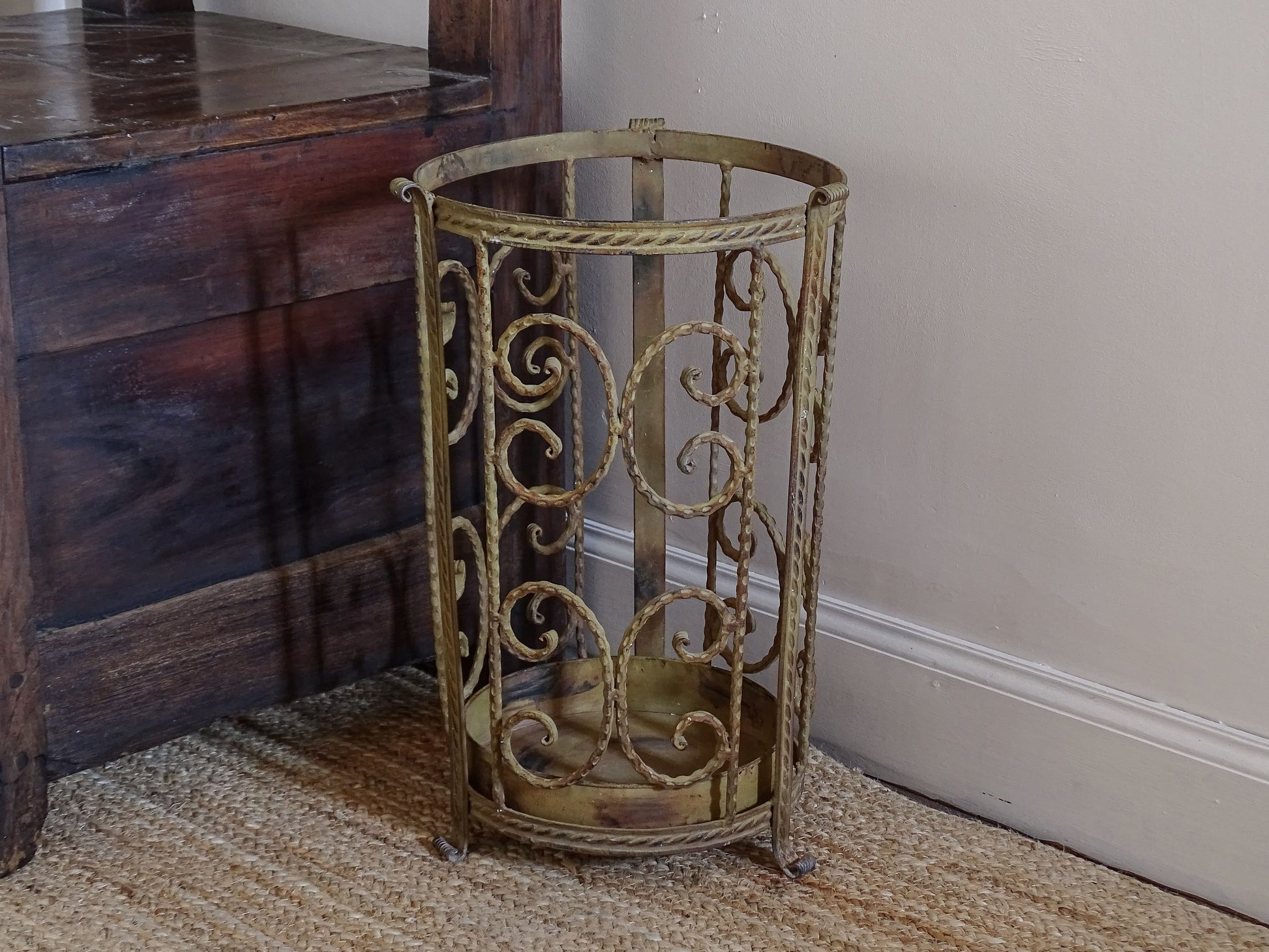 Decorative French umbrella stand in distressed painted metal beside rustic wooden furniture