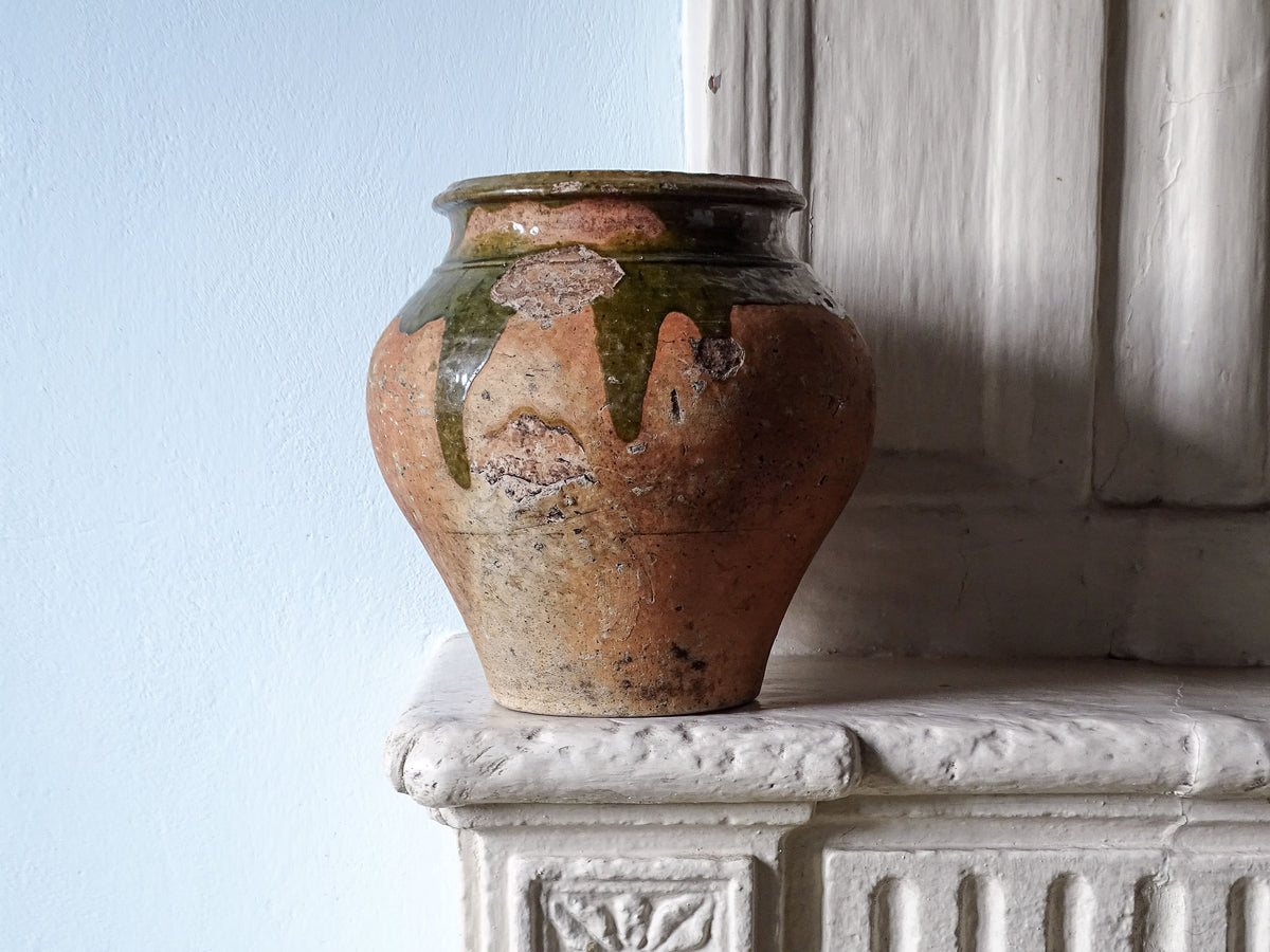 French antique earthenware pot with dark green glaze, displayed on a country house fireplace