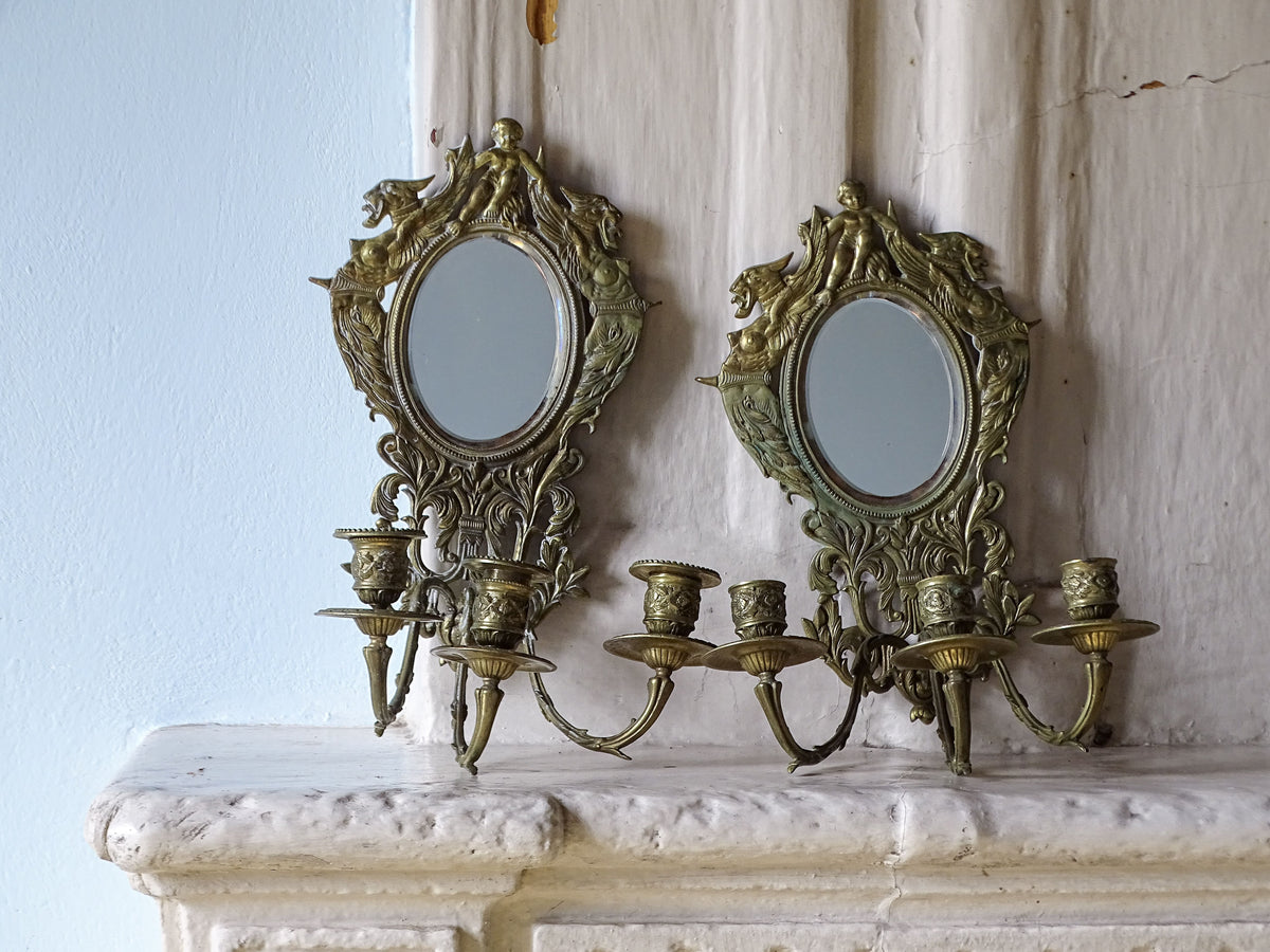 Pair of ornate French antique brass candle sconce mirrors with griffon and cherub decoration. Pictured on a country house fireplace.