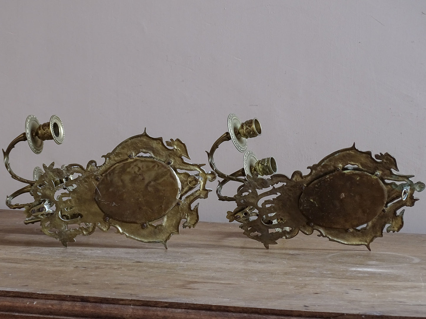 Detail of French antique mirror sconce featuring griffin decoration and cherub above an oval mirror.