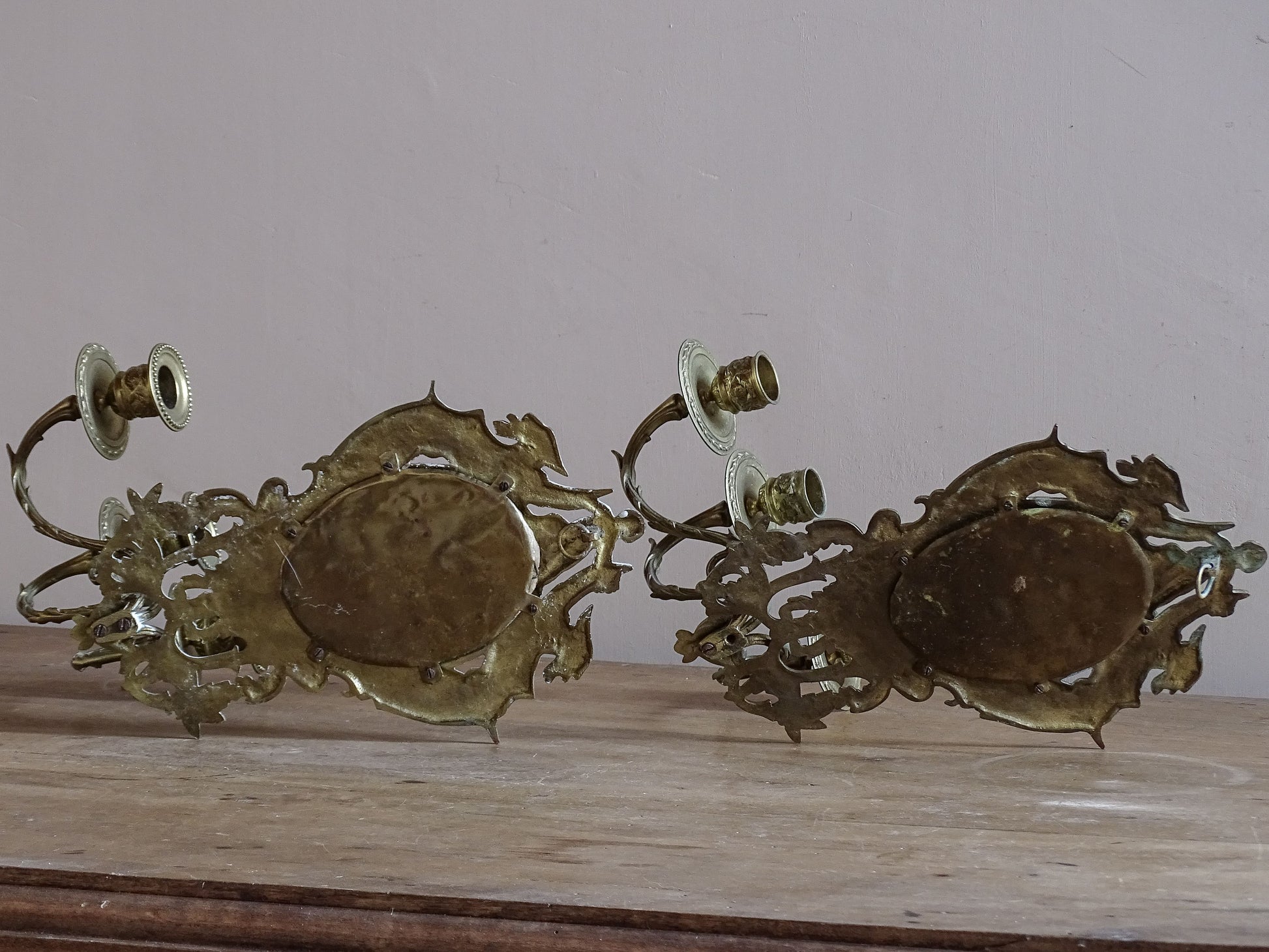 Detail of French antique mirror sconce featuring griffin decoration and cherub above an oval mirror.