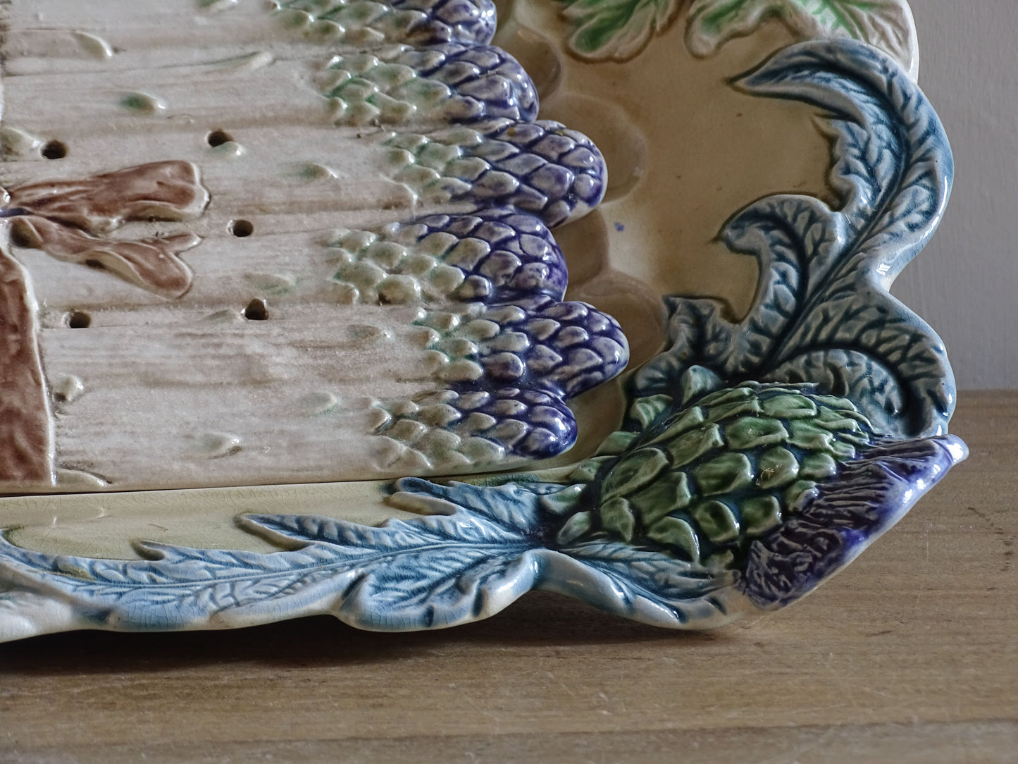 Decorative French majolica asparagus dish with raised artichoke motif and cream glazed interior.