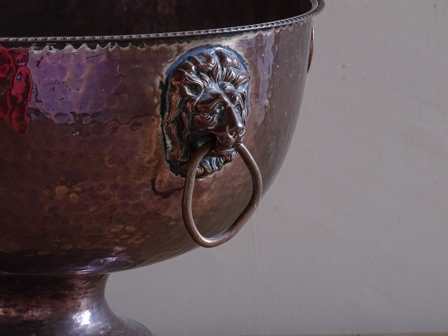 Decorative antique copper ice bucket with lion head handles and pedestal foot.