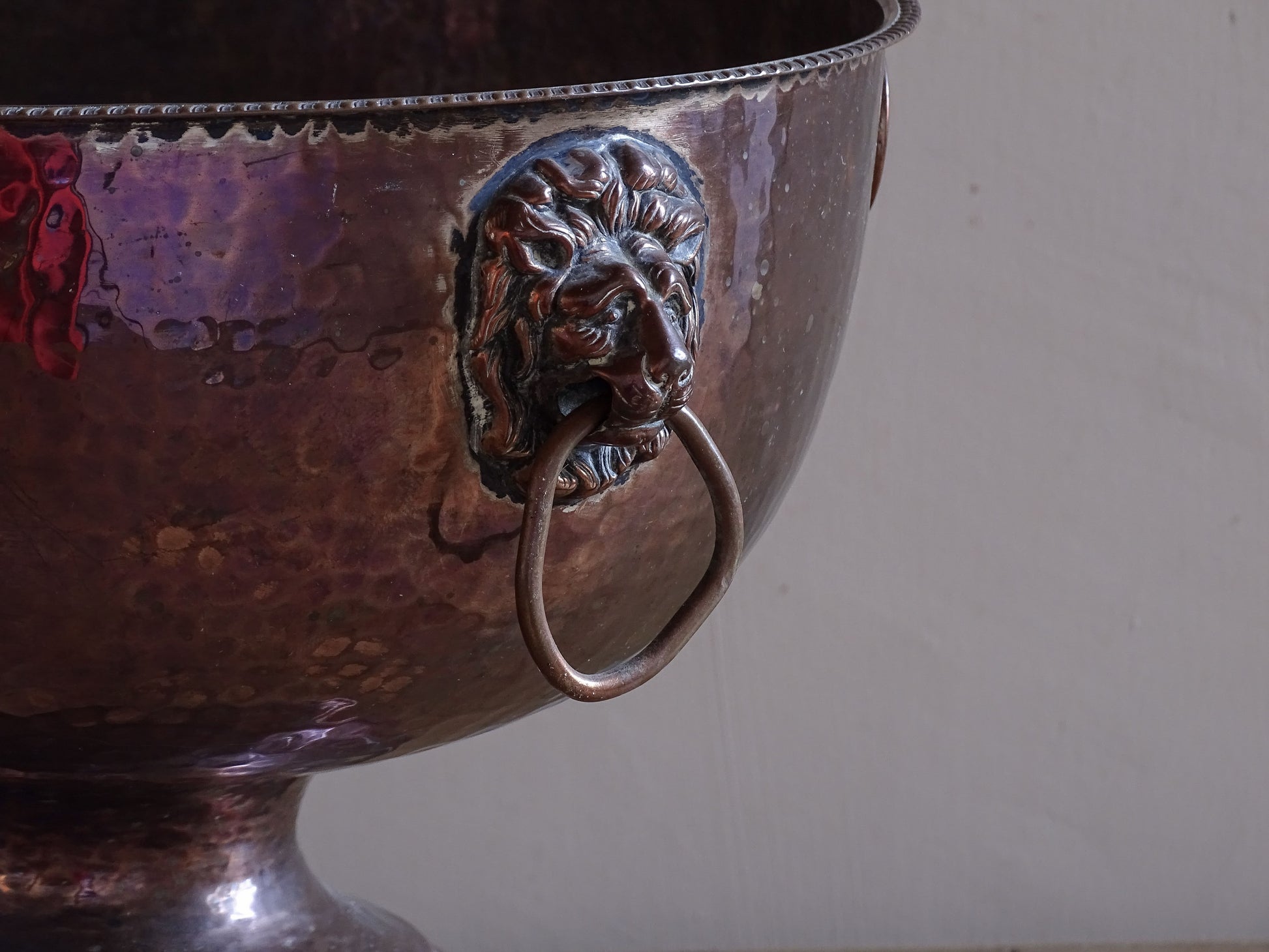 Decorative antique copper ice bucket with lion head handles and pedestal foot.