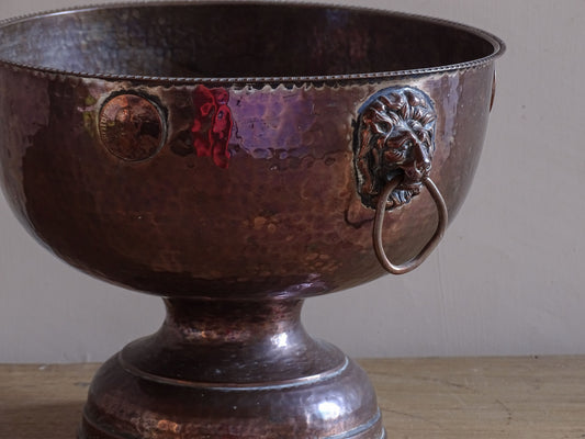 Antique hammered copper wine cooler with lion head ring handles and pedestal base.