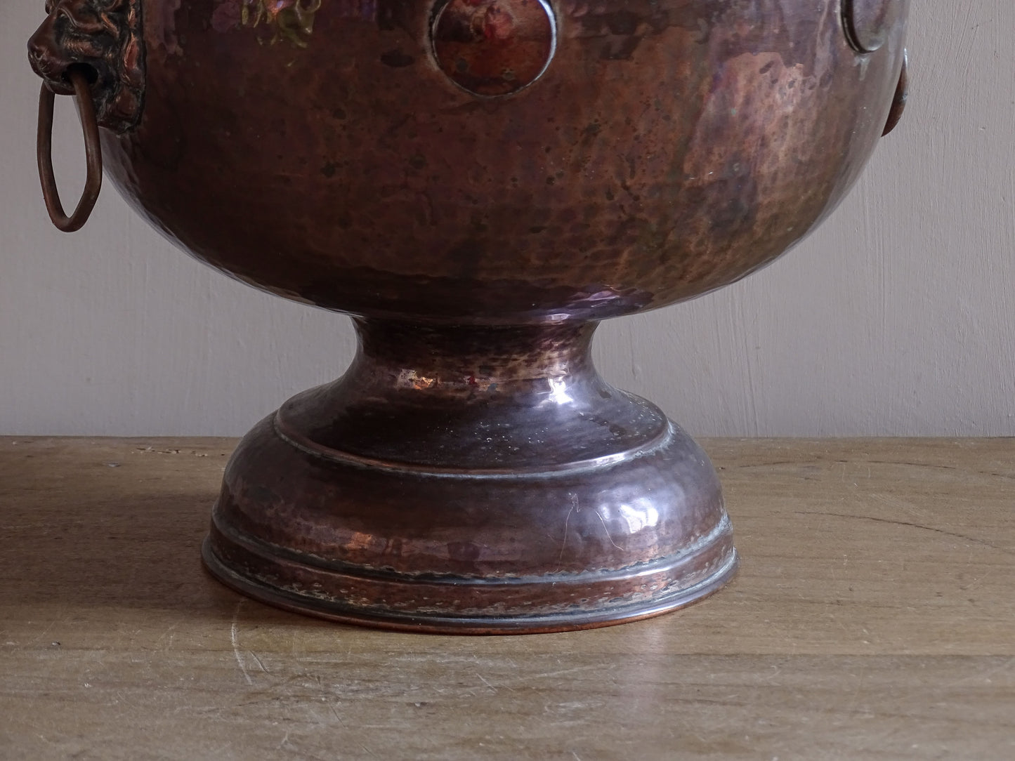 Antique hammered copper vessel with lion mask ring handles and decorative roundels.