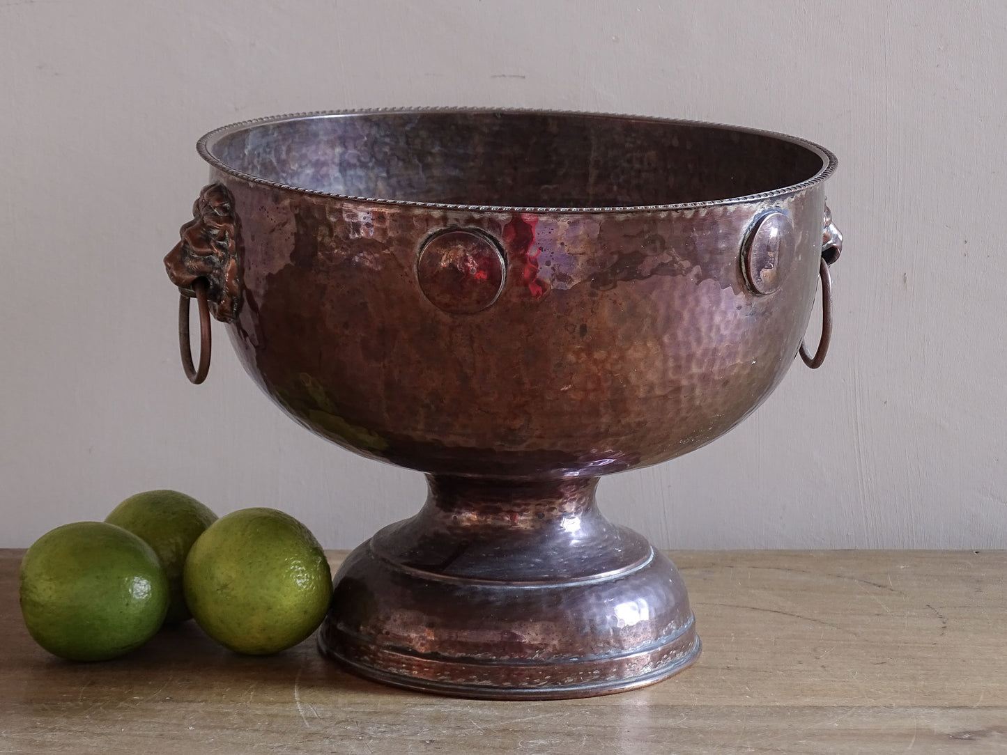 Antique hammered copper wine cooler with lion head ring handles and pedestal base.