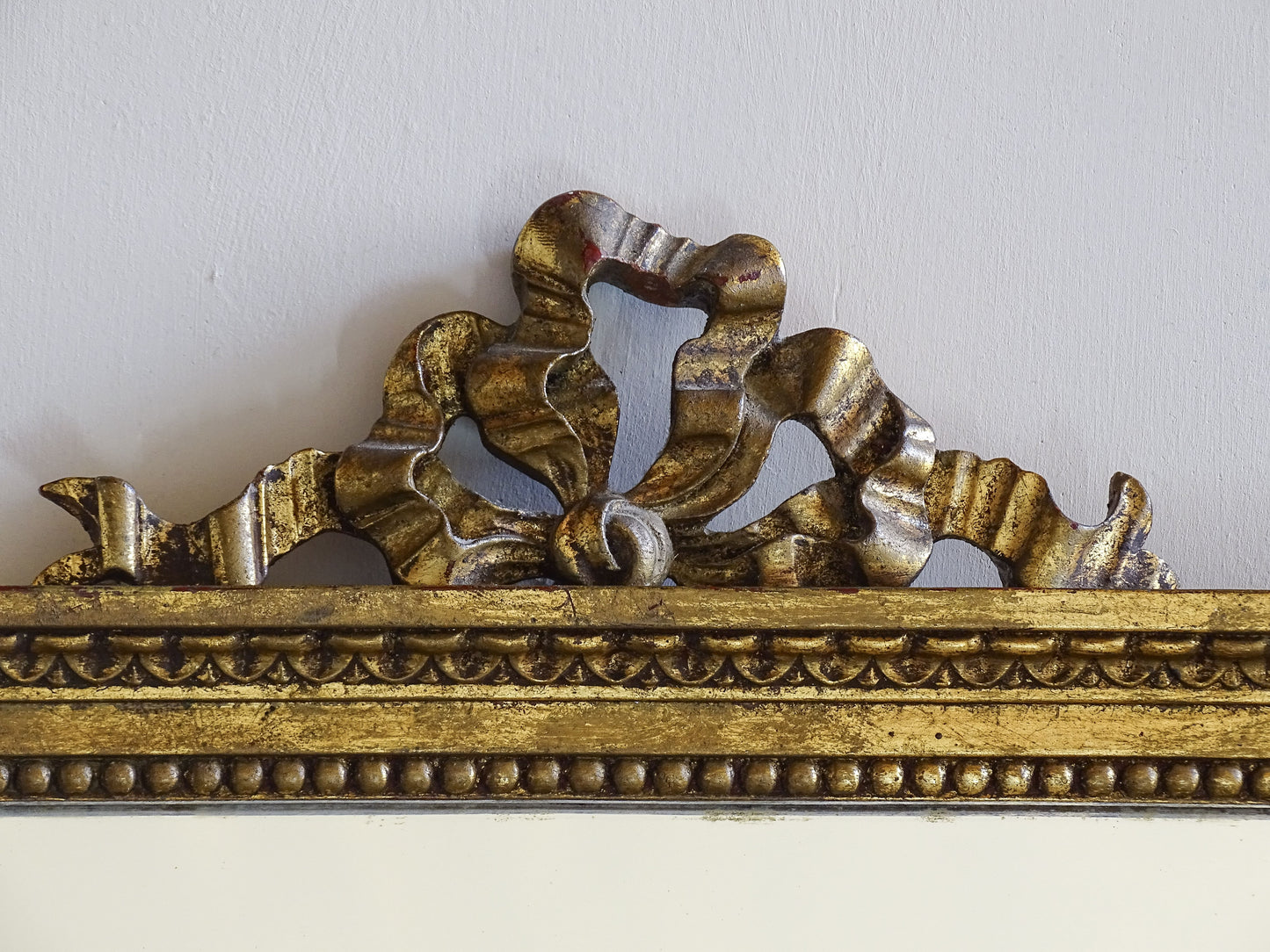 French gilt mirror with ribbon crest and foxed glass in a neoclassical style frame