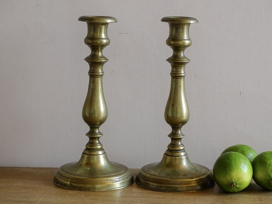 Pair of antique brass candlesticks with aged patina on a wooden table.