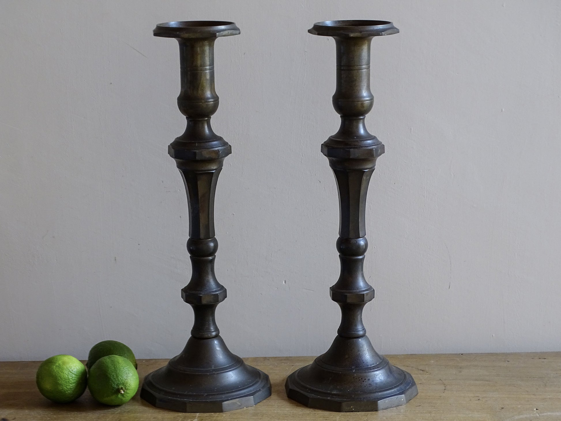 Pair of tall antique altar candlesticks displayed with green limes for scale
