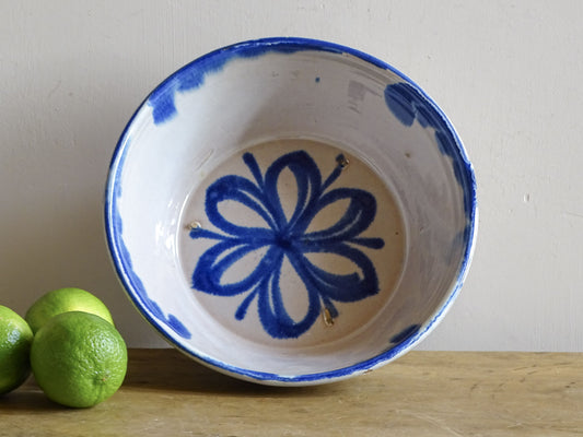 Spanish Fajalauza lebrillo bowl displayed with green limes, showing its blue floral interior and white glaze.