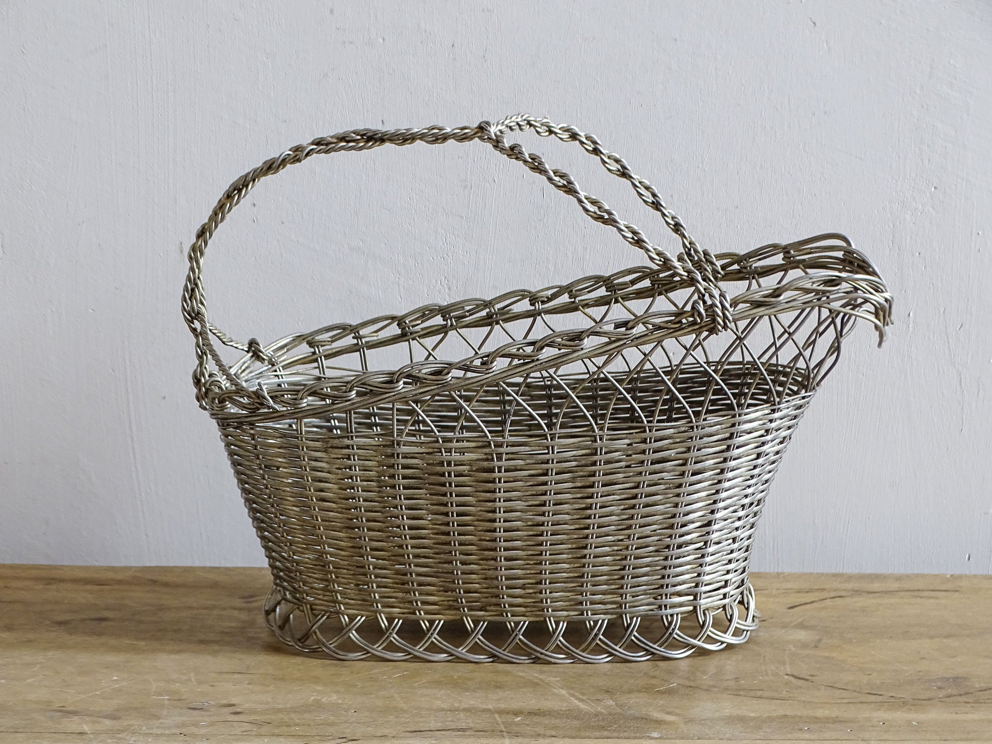 French vintage wire wine bottle carrier with twisted handle, displayed on a rustic wooden table.
