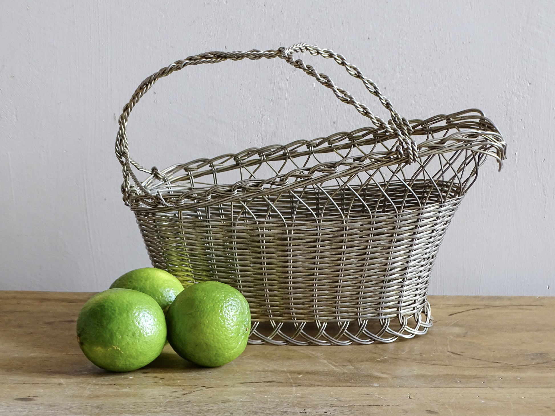 French vintage wire wine bottle carrier with twisted handle, displayed on a rustic wooden table with three green limes.
