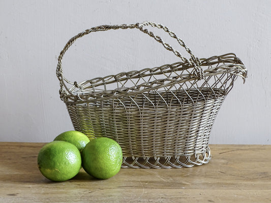 French vintage wire wine bottle carrier with twisted handle, displayed on a rustic wooden table with three green limes.